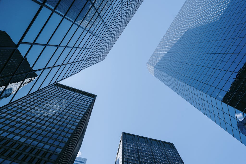 Upward angle of tall, glass skyscrapers with a clear blue sky, emphasizing modern architecture.